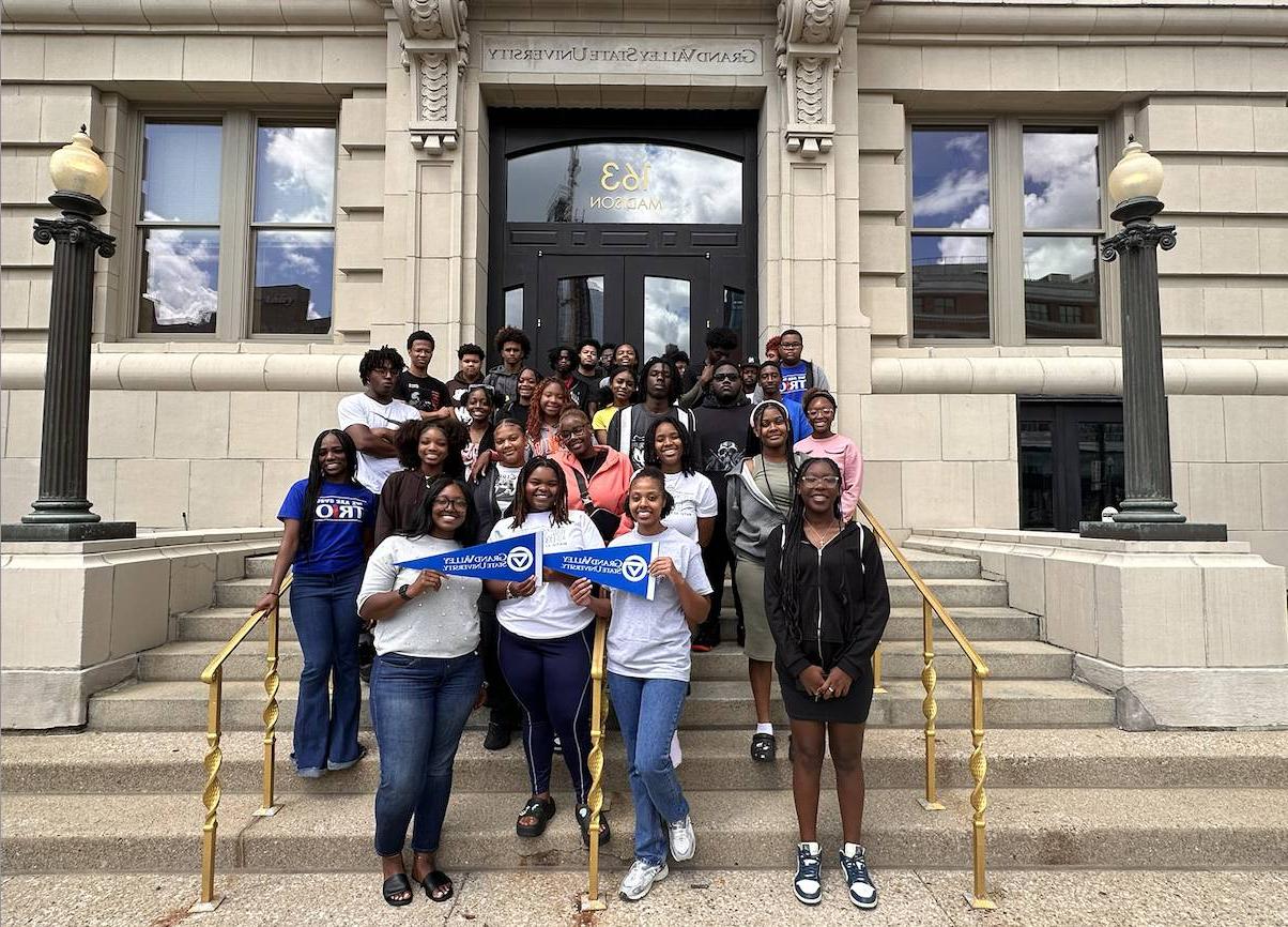 Group photo of students holding GV flags standing in front of GVSU Detroit campus building